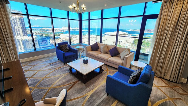 A spacious living room with a large window offering a city view, a sofa, two armchairs, and a coffee table. - Sherao Hotel Doha - Next to National Museum of Qatar & Metro (Doha)