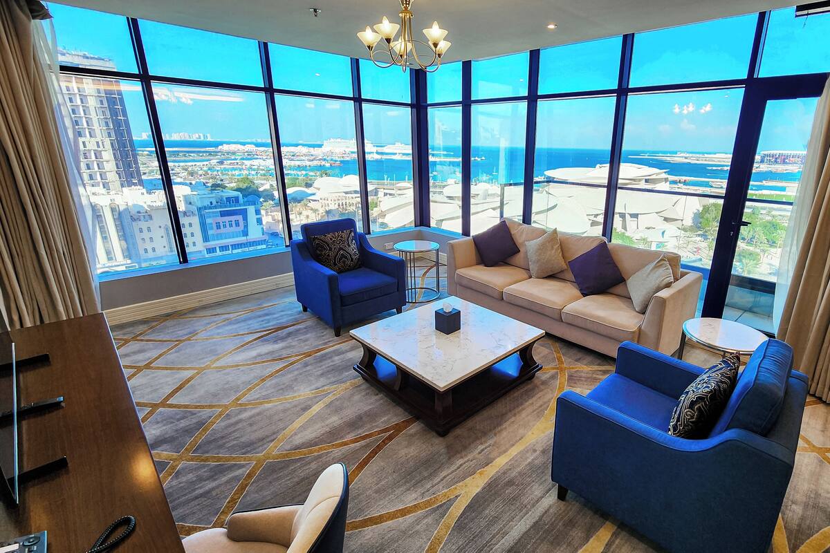 A spacious living room with a large window offering a city view, a sofa, two armchairs, and a coffee table.