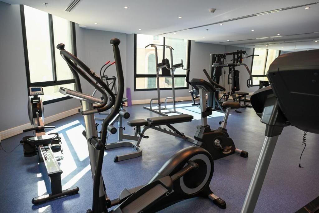 Un gimnasio con máquinas de cardio, pesas libres y una banca.