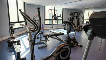 Un gimnasio con máquinas de cardio, pesas libres y una banca.