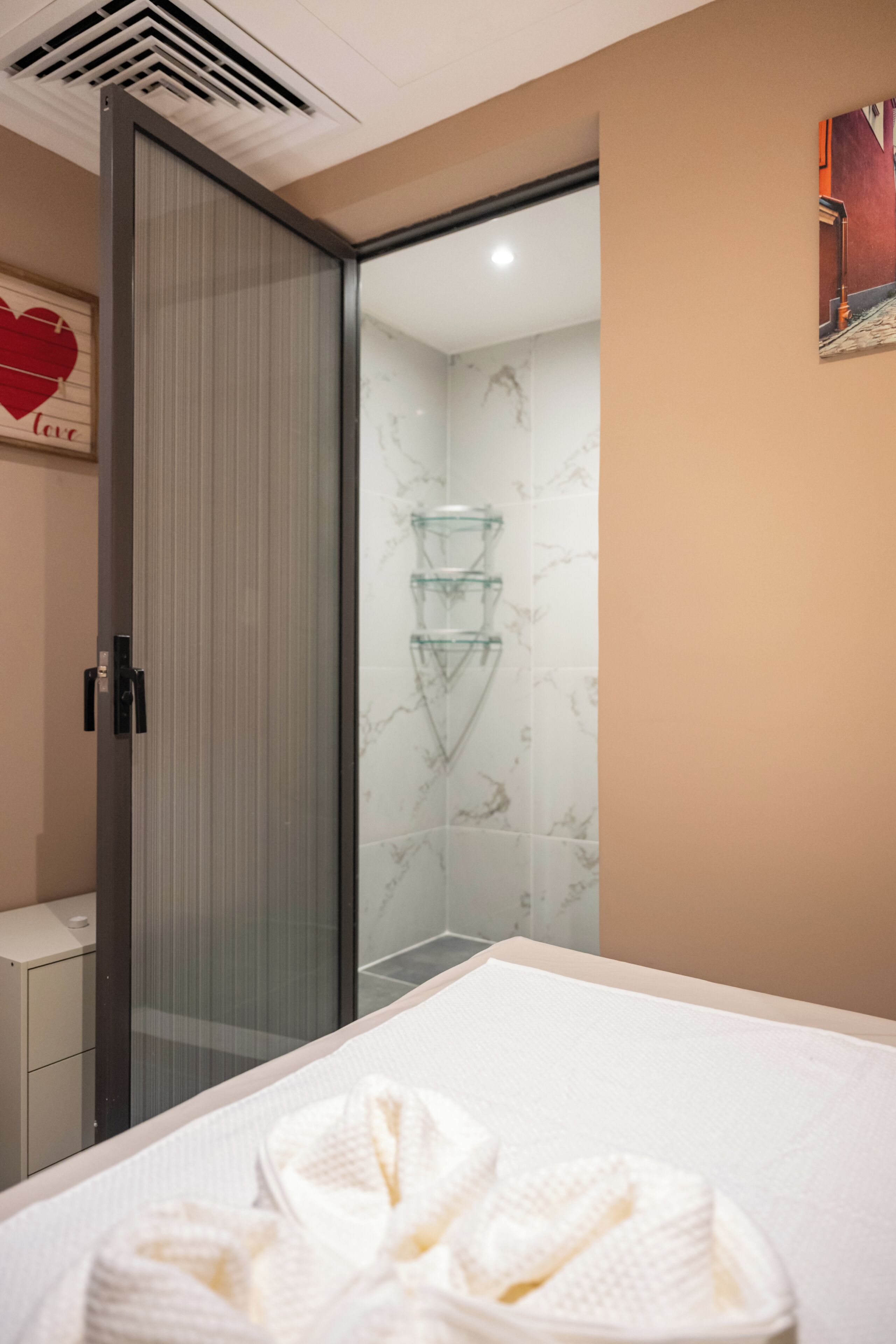 A hotel room with a bed, a glass shower enclosure, and a towel on the bed.