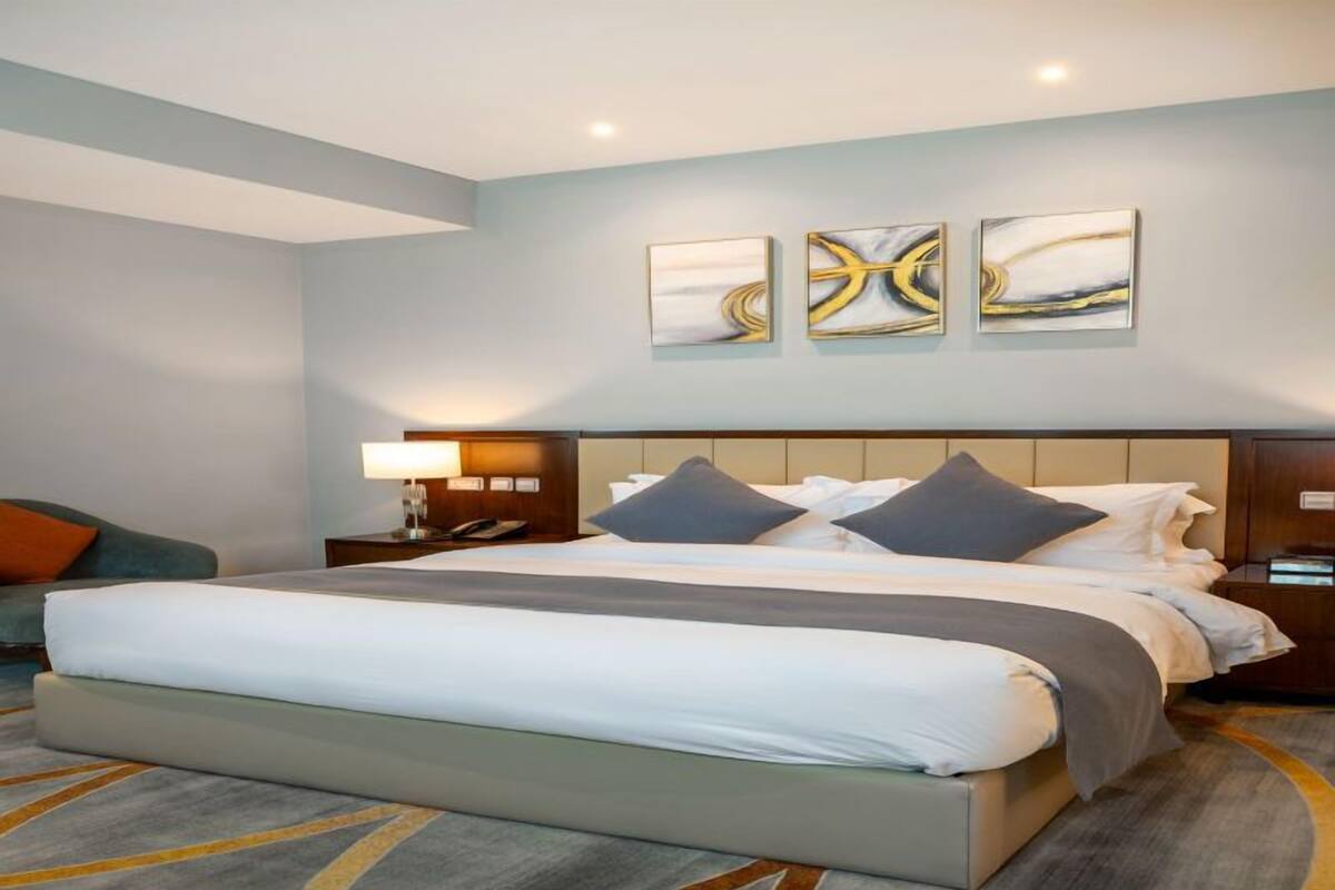 A hotel room with a large bed, a nightstand, a lamp, and three abstract paintings on the wall.