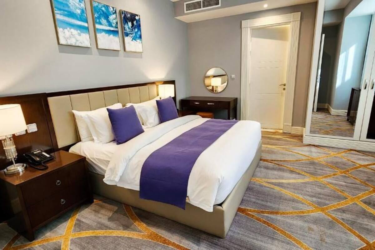 A hotel room with a bed, nightstand, bedside table, and a large mirror.