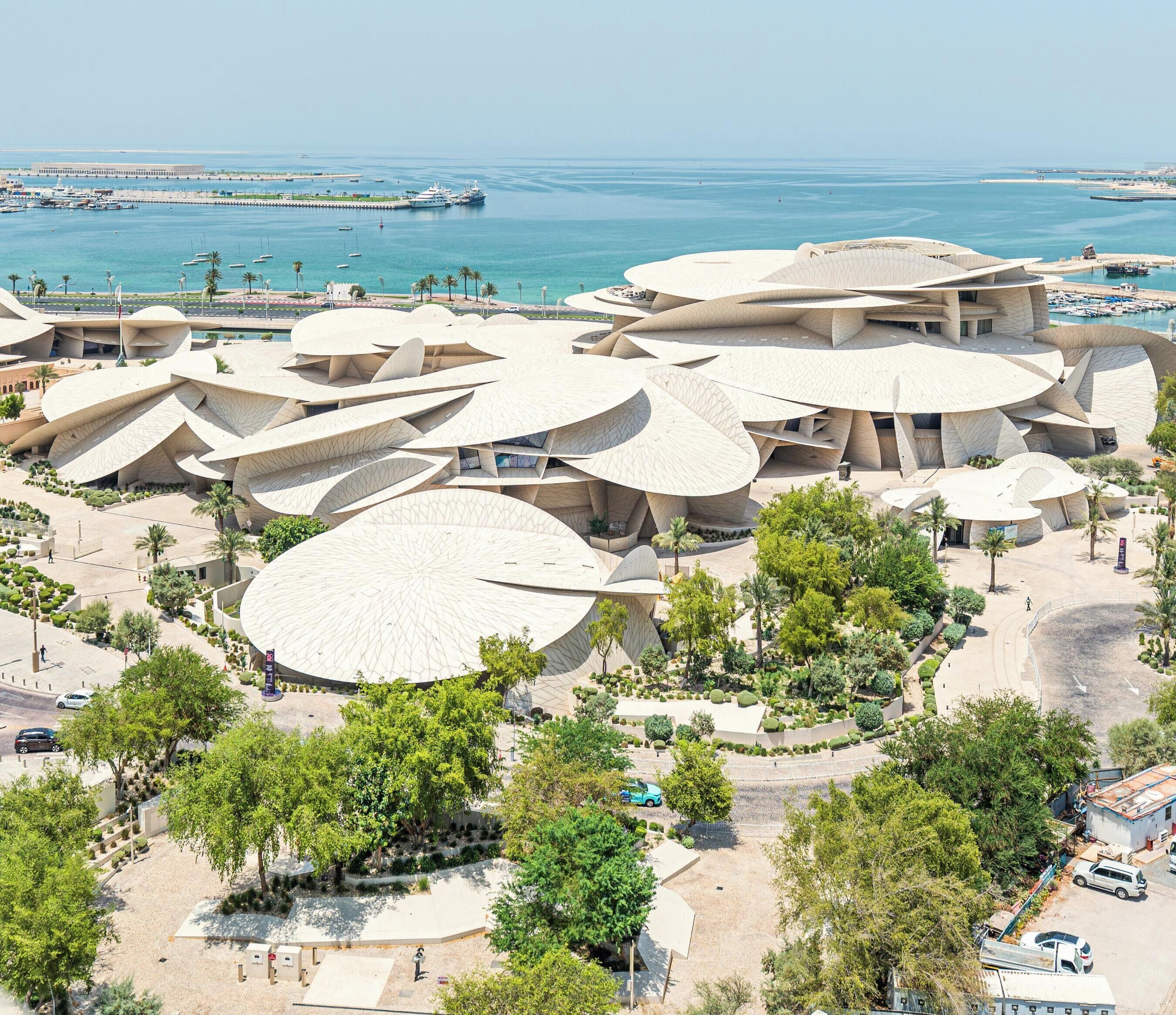 Un moderno complejo arquitectónico con varias construcciones interconectadas, una marina con barcos y una vista despejada del mar.