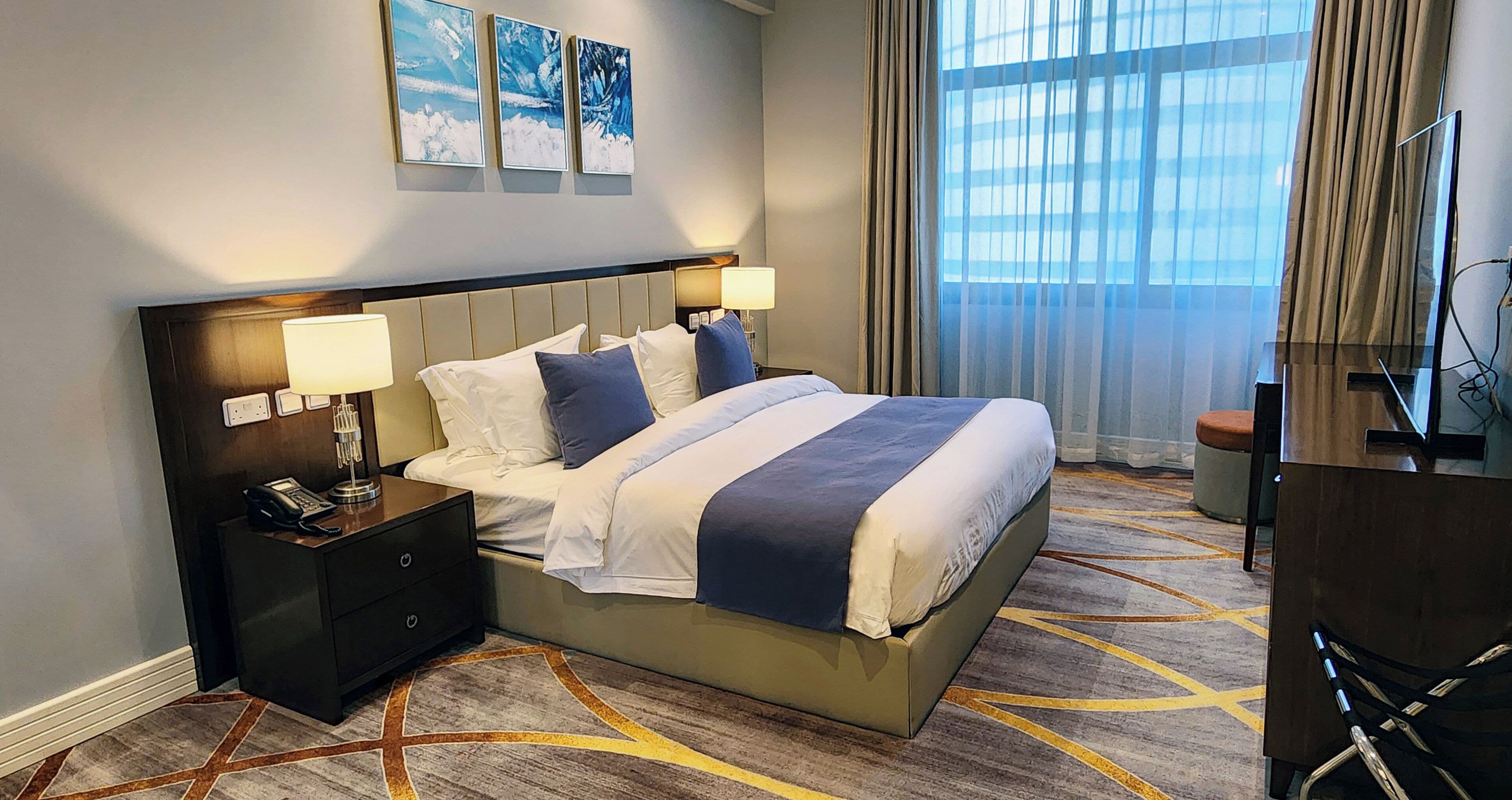 A hotel room with a large bed, two bedside tables with lamps, a desk, and a chair.