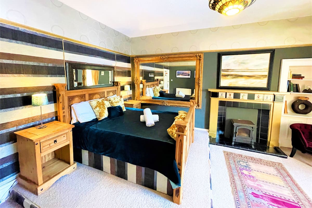 A bedroom with a bed, bedside tables, a mirror, a fireplace, and a rug.