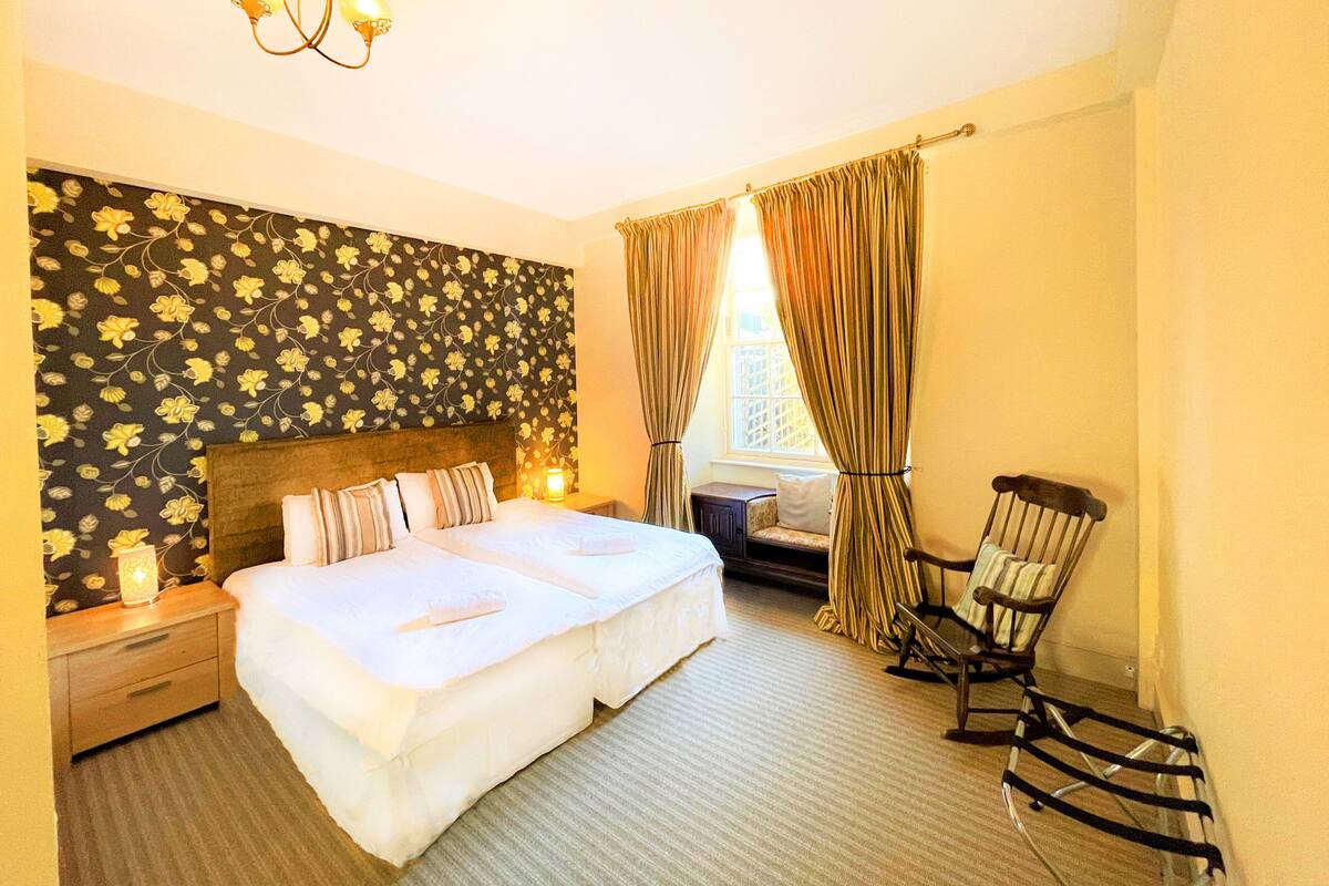 A hotel room with a large bed, a nightstand, a chair, and a window with curtains.