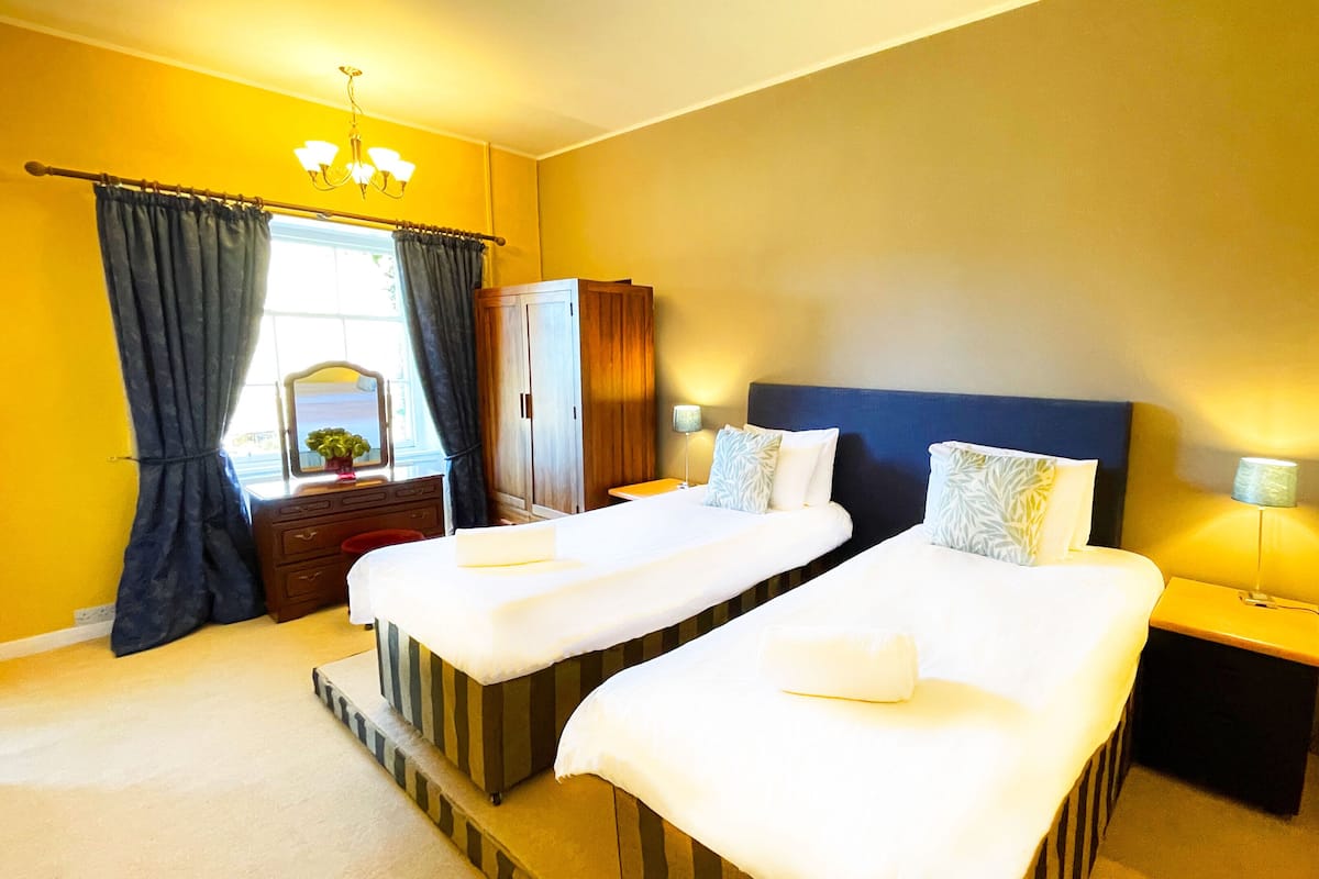 A hotel room with two beds, a dresser, a mirror, a wardrobe, and a window with curtains.