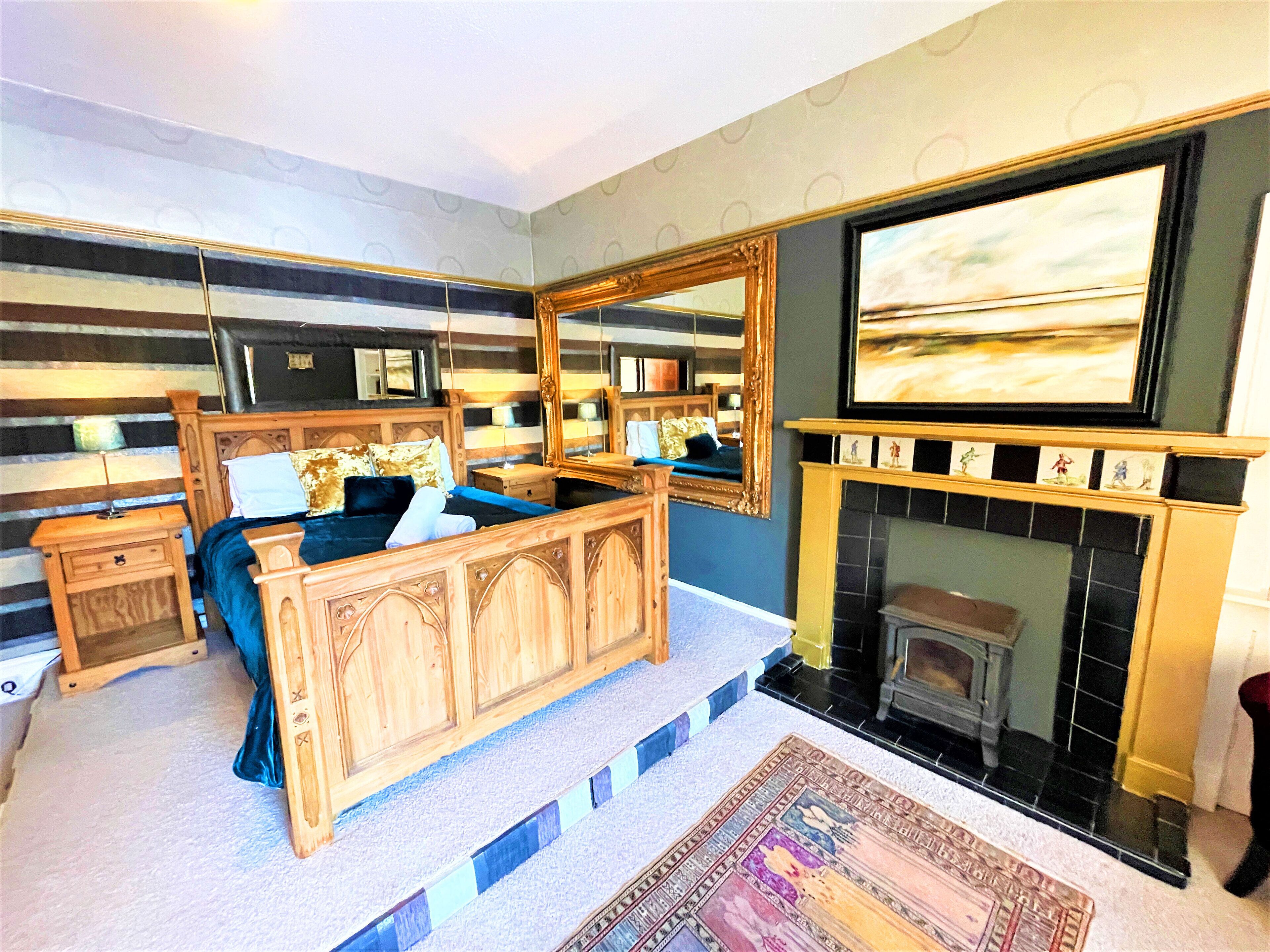 A bedroom with a large bed, a fireplace, and a large mirror.