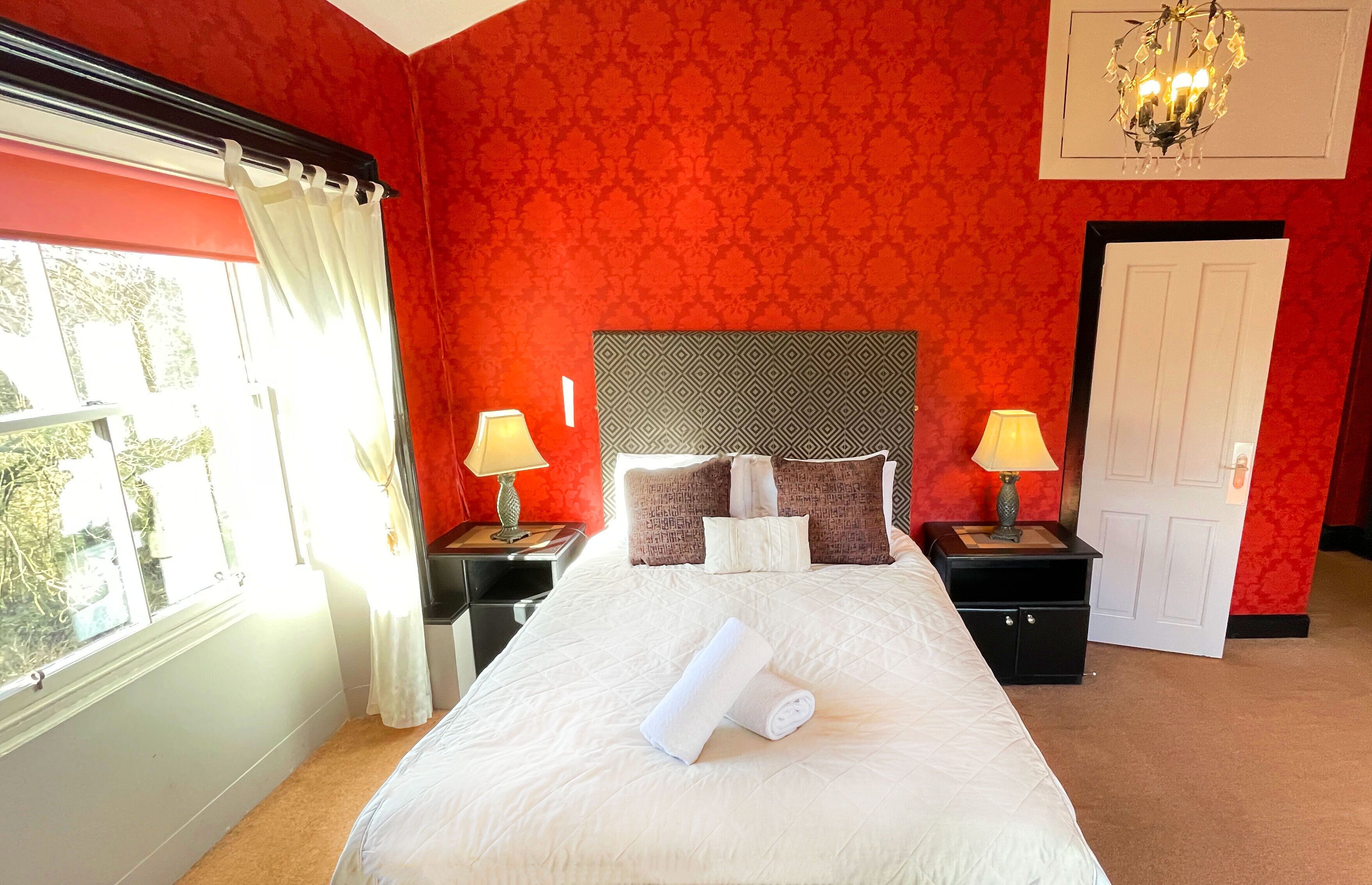 A hotel room with a large bed, two bedside tables with lamps, a headboard, and a window with curtains.