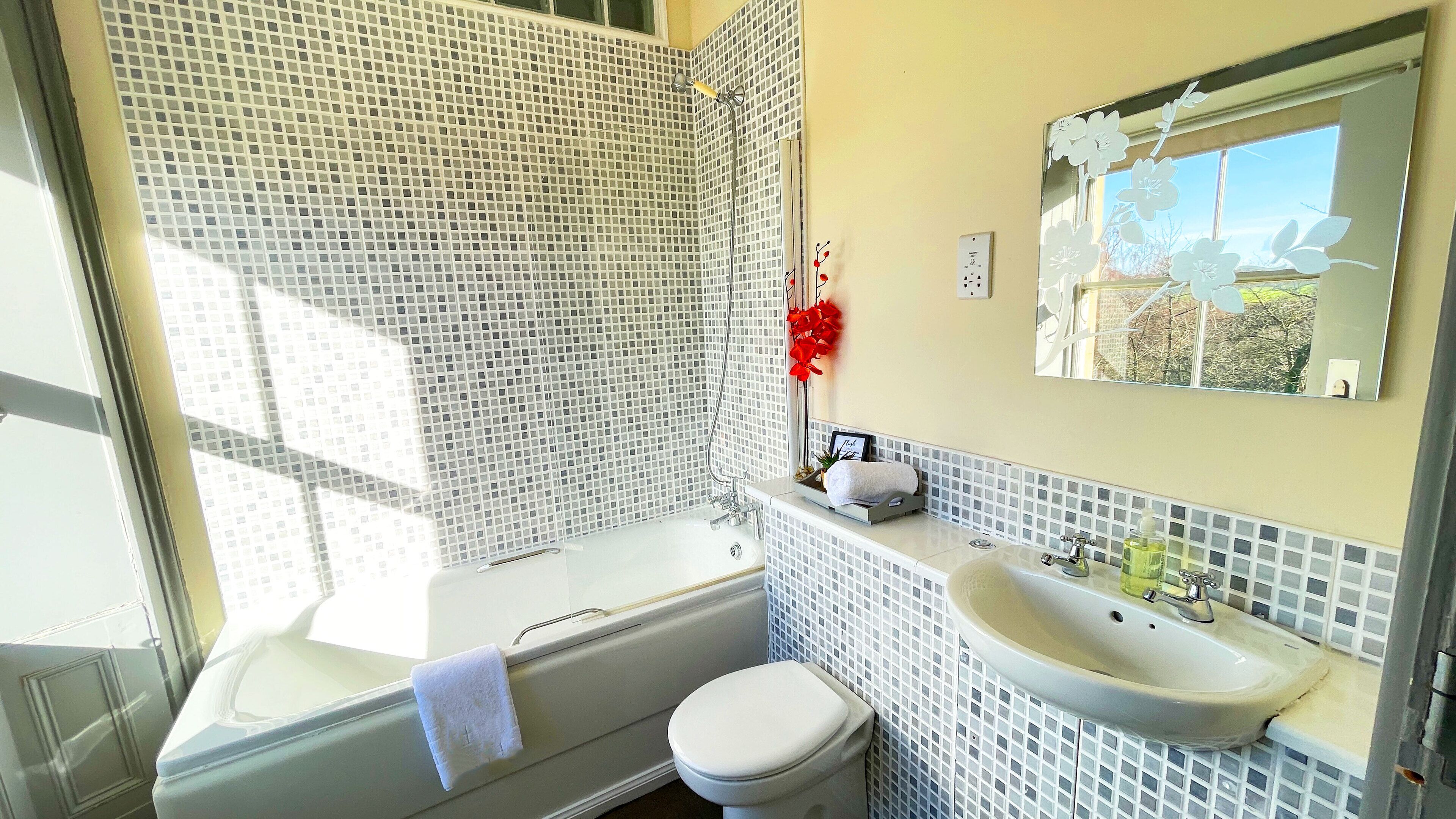 Un baño con bañera, inodoro y lavamanos, con un salpicadero de azulejos y una ventana con vistas.