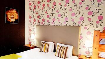Ein Hotelzimmer mit einem großen Bett, zwei Nachttischen, einem hölzernen Kopfteil, blumigem Wandpapier und einem gerahmten Bild an der Wand.