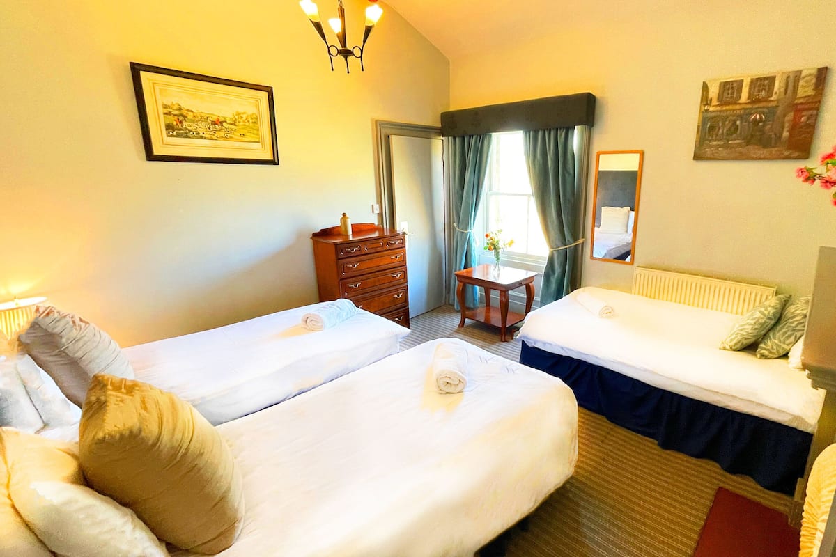 A hotel room with two beds, a dresser, a table with a vase of flowers, and a mirror on the wall.