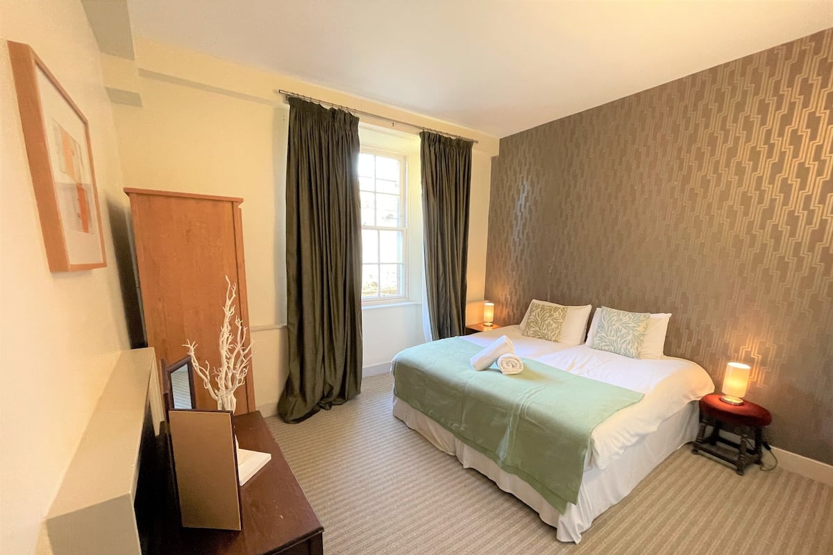 A bedroom with a bed, a nightstand, a dresser, and a window with curtains.