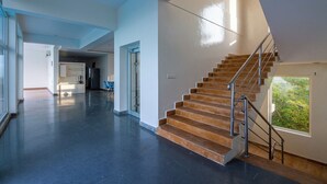 A spacious interior with a central staircase, a kitchen area, and a view of greenery outside.