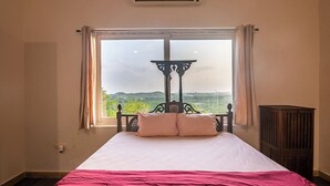 A bed with a view of a landscape through a window, a bedside table, and a radiator.