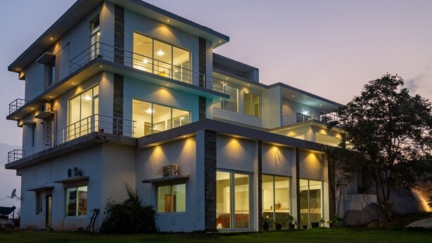 A modern multi-story house with large windows, balconies, and outdoor lighting.