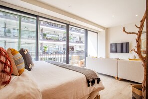Habitación de hotel moderna con una cama grande, televisor y balcón con vistas a la ciudad.