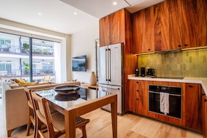 Una cocina moderna con armarios de madera, un refrigerador de acero inoxidable y un comedor con mesa y sillas de vidrio.