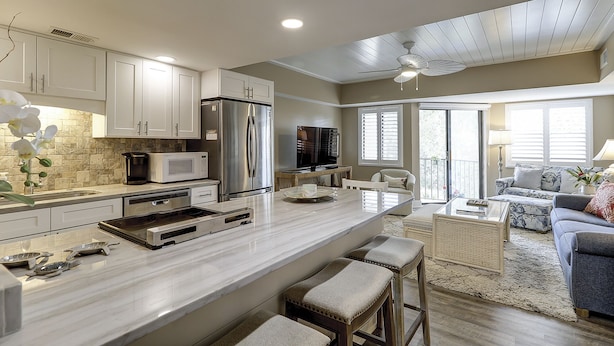 A modern kitchen with a large island, stainless steel appliances, and a dining area with a glass table. - Sunset Rentals | Forest Beach Villa 415 (Hilton Head Island)