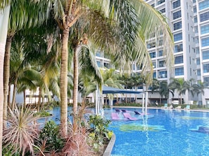 Una piscina rodeada de palmeras y un edificio moderno con balcones.