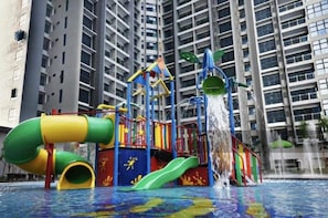Un área de juegos acuáticos con toboganes y estructuras para escalar, rodeada de edificios residenciales altos.