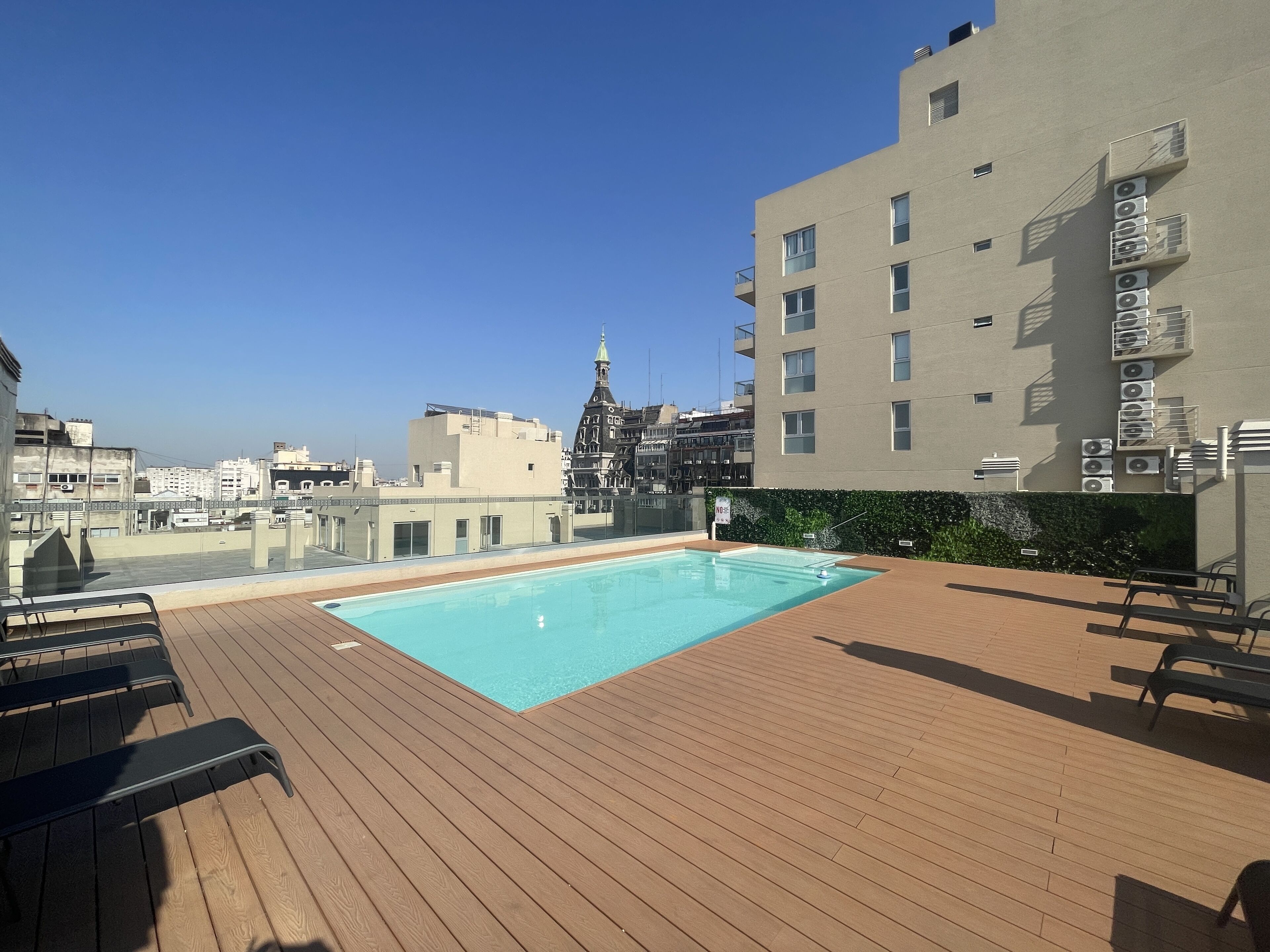 A rooftop pool area with a wooden deck, a pool, and a view of the cityscape.