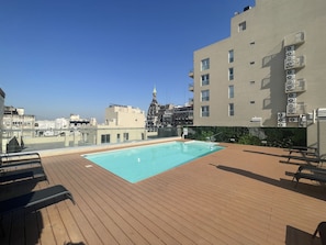 Un área de piscina en la azotea con terraza de madera, piscina y vista panorámica de la ciudad.