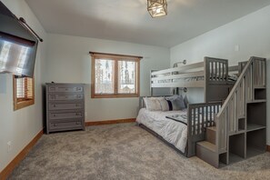 Une chambre avec un lit superposé, une commode, une fenêtre avec des stores et un luminaire au plafond.