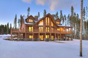 Un grand chalet en bois doté de nombreux balcons et de grandes fenêtres, entouré de neige et d’arbres.