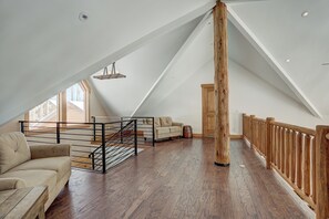 A spacious loft with a high ceiling, a wooden staircase, a sofa, and a view of the outside. - Big Blue Trace (Breckenridge)
