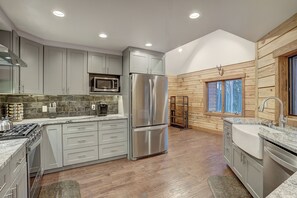 A modern kitchen with grey cabinets, stainless steel appliances, and a wooden wall. - Big Blue Trace (Breckenridge)