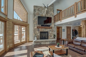 A spacious living area with a stone fireplace, wooden flooring, and a leather sofa.