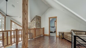 A spacious loft with a high ceiling, wooden flooring, a stone accent wall, and a view of the outdoors. - Big Blue Trace (Breckenridge)