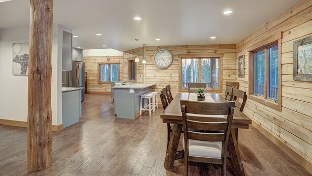 Une cuisine spacieuse aux murs en bois, un coin repas avec une table et des chaises en bois, et une grande horloge au mur.