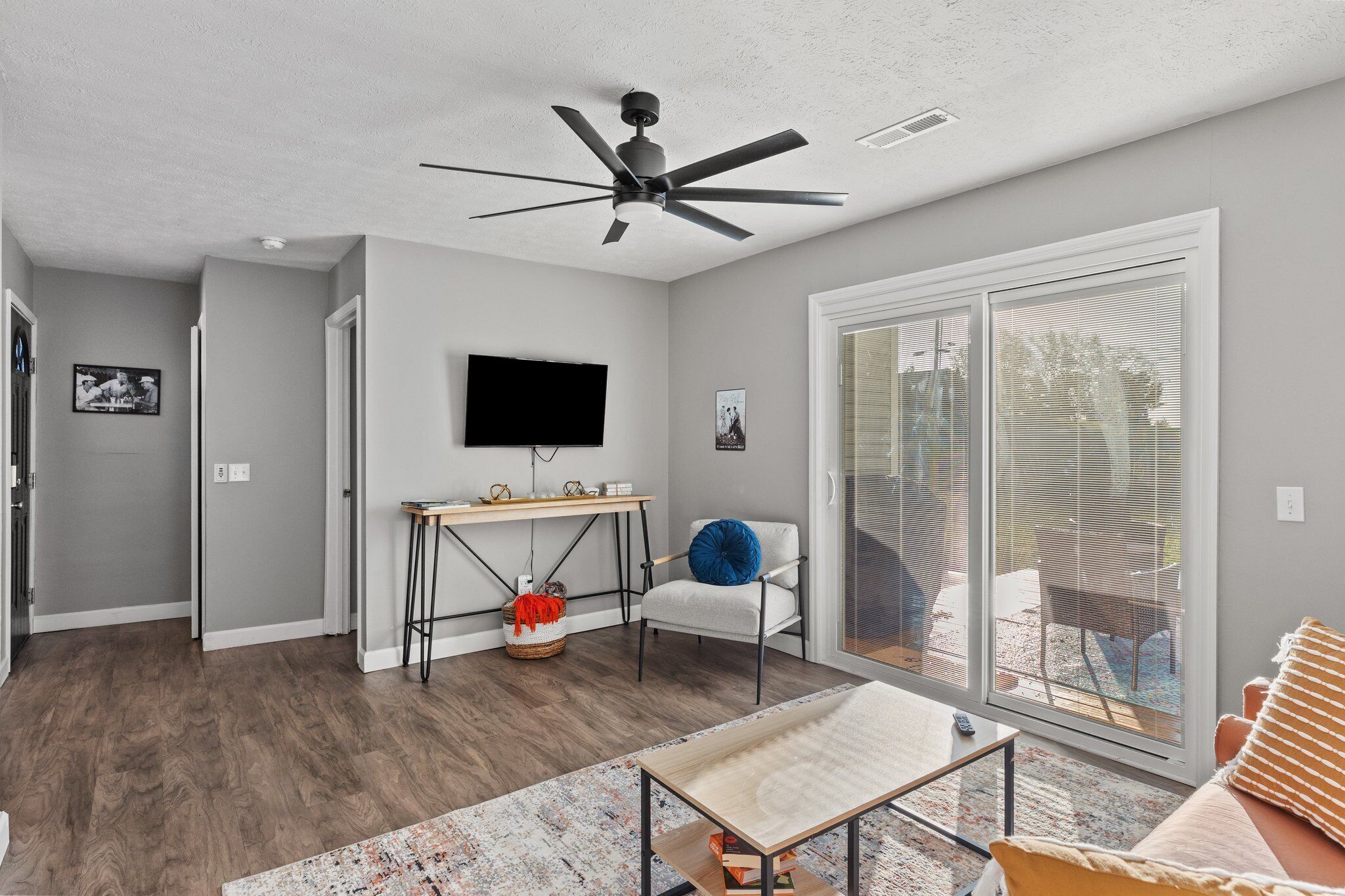 Een moderne woonkamer met een plafondventilator, een flatscreen televisie, een eethoek met een tafel en stoelen, en een grote schuifdeur die leidt naar een buiten terras.