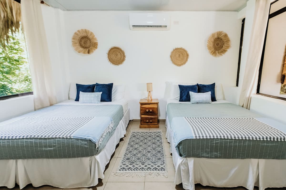 A double room with two beds, a small wooden nightstand, and a patterned rug.