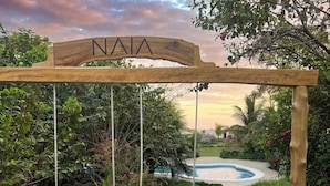 Un pont-levis en bois enjambe un étang, avec une piscine en arrière-plan.
