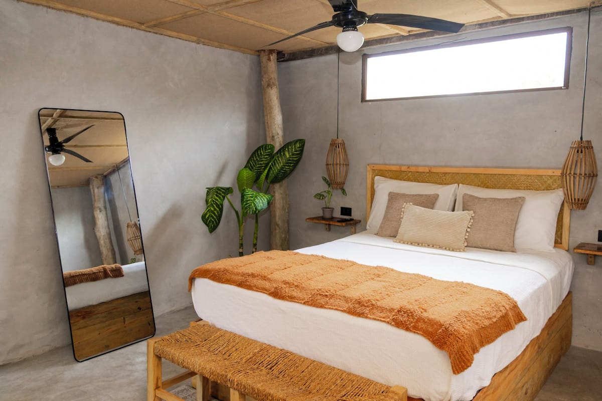A bedroom with a bed, a ceiling fan, a large mirror, and a window.