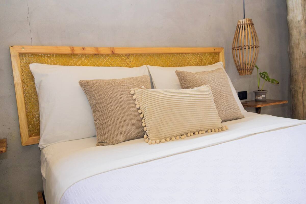 A neatly made bed with a wooden headboard, two pillows, and a bedside table with a plant.