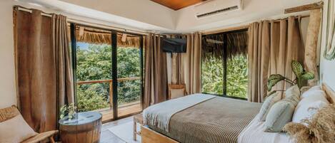 A bedroom with a large bed, wooden flooring, a TV, and a balcony with curtains.