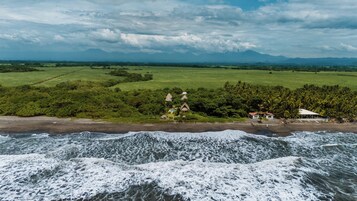 A coastal landscape with a beach, ocean waves, and a small settlement with thatched-roof houses.