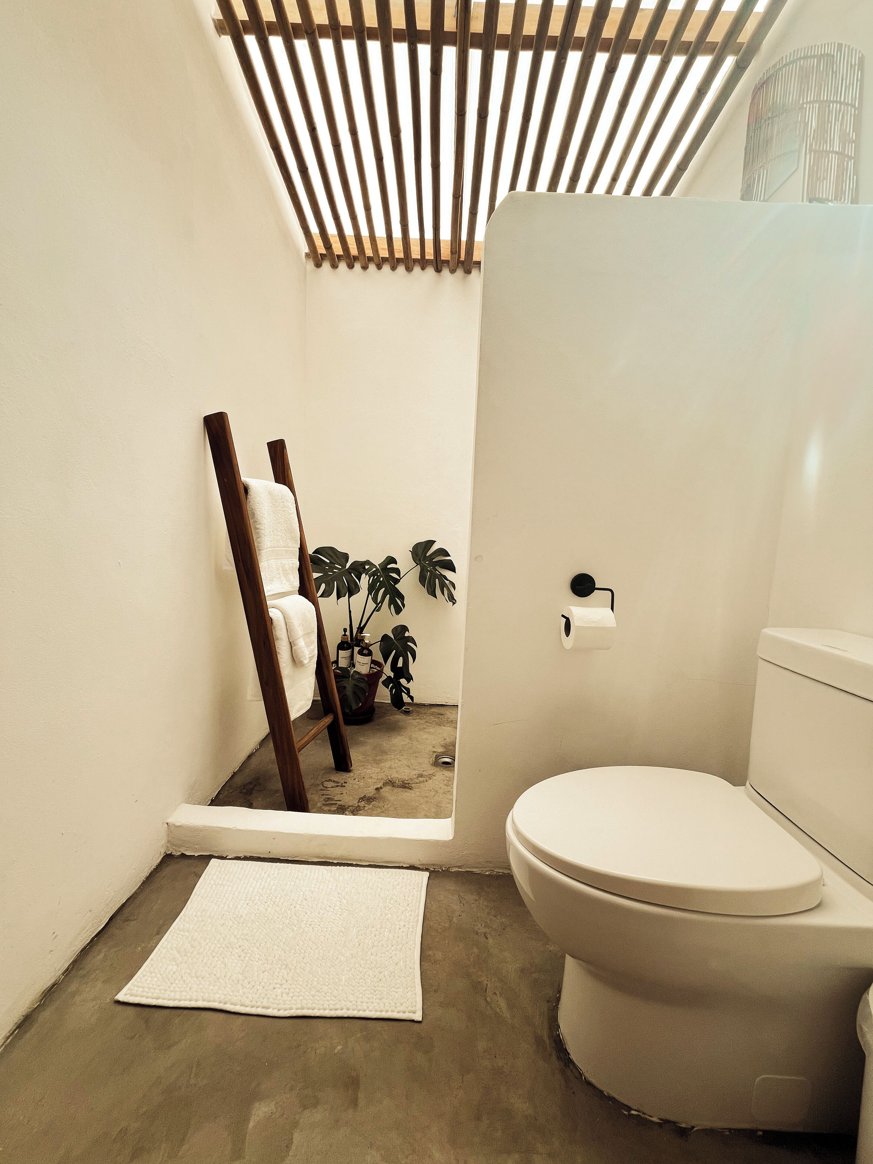 A compact bathroom with a toilet, a small sink, a towel rack, and a wooden chair.