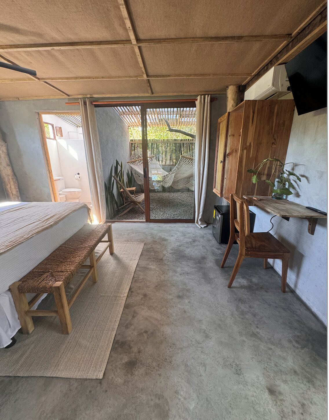Una habitación pequeña con cama, escritorio y una hamaca.