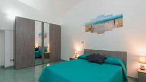A bedroom with a bed, a wardrobe, a nightstand, and a wall-mounted lamp. - 1 Bedroom Apartment in Ischia (Ischia)