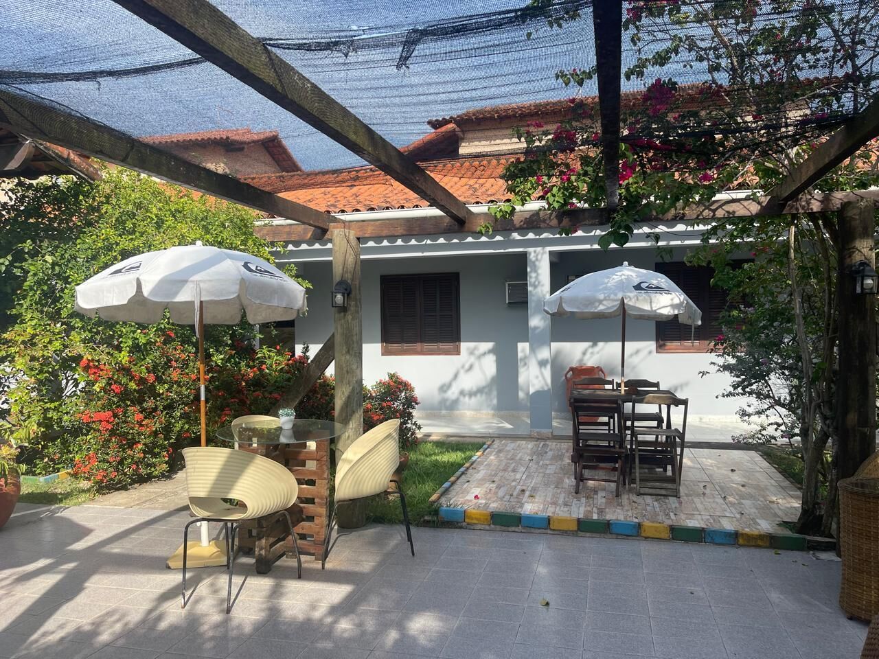 An outdoor patio with a table and chairs, surrounded by potted plants and a pergola.