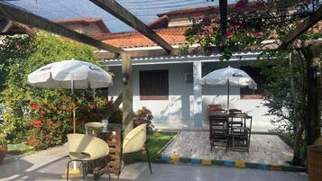 An outdoor patio with a table and chairs, surrounded by potted plants and a pergola.