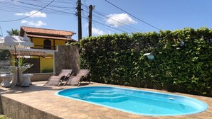 Una piscina con bordeado de baldosas, sillas de descanso y un edificio al fondo.