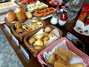 A buffet table with various food items including bread, pastries, and sliced fruits. - Pousada do Suiço (Saquarema)