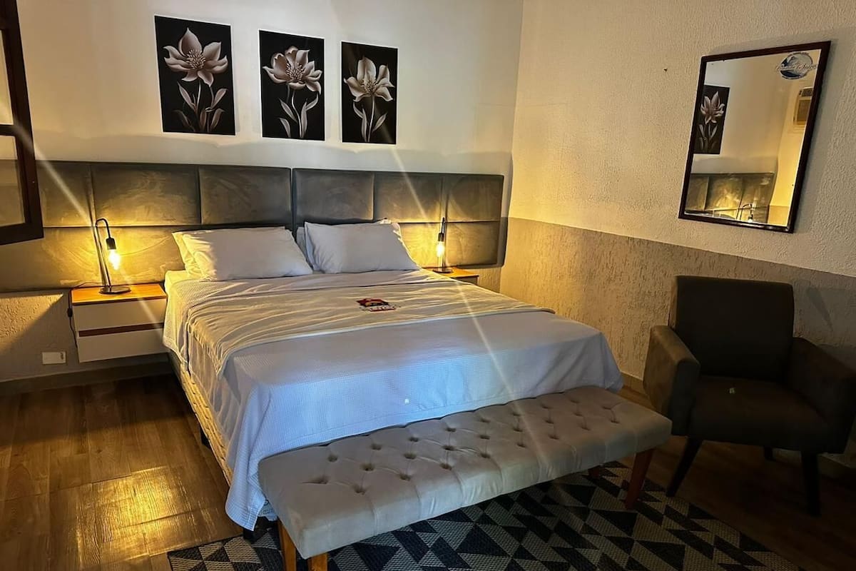 A bedroom with a bed, bedside tables, a bench, a chair, and wall art.